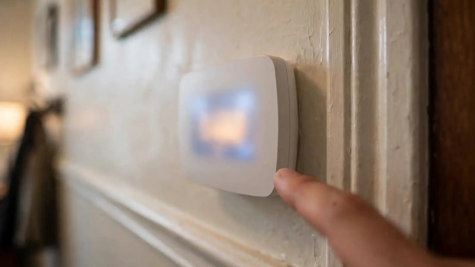 Hand adjusting a thermostat on a hallway wall